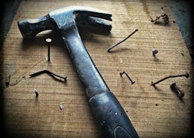 A weathered hammer surrounded by bent nails on a wooden plank, capturing the essence of carpentry work.